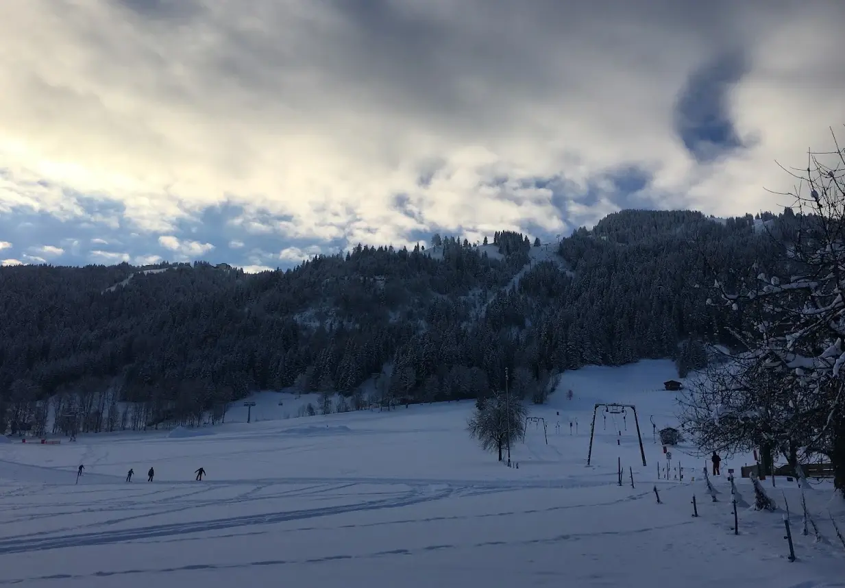 Winter day on the practice slope with a drag lift, cross-country skiers and wooded slopes behind
