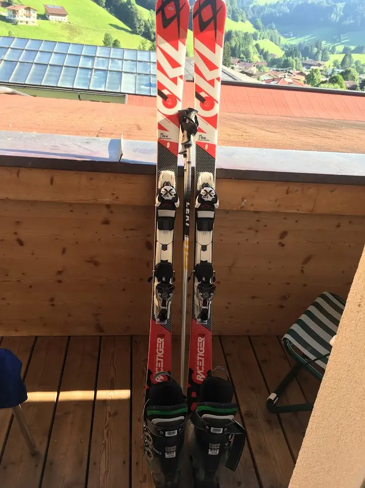 Skis, ski pole and ski boots on a wooden balcony overlooking green meadows and villages in the valley