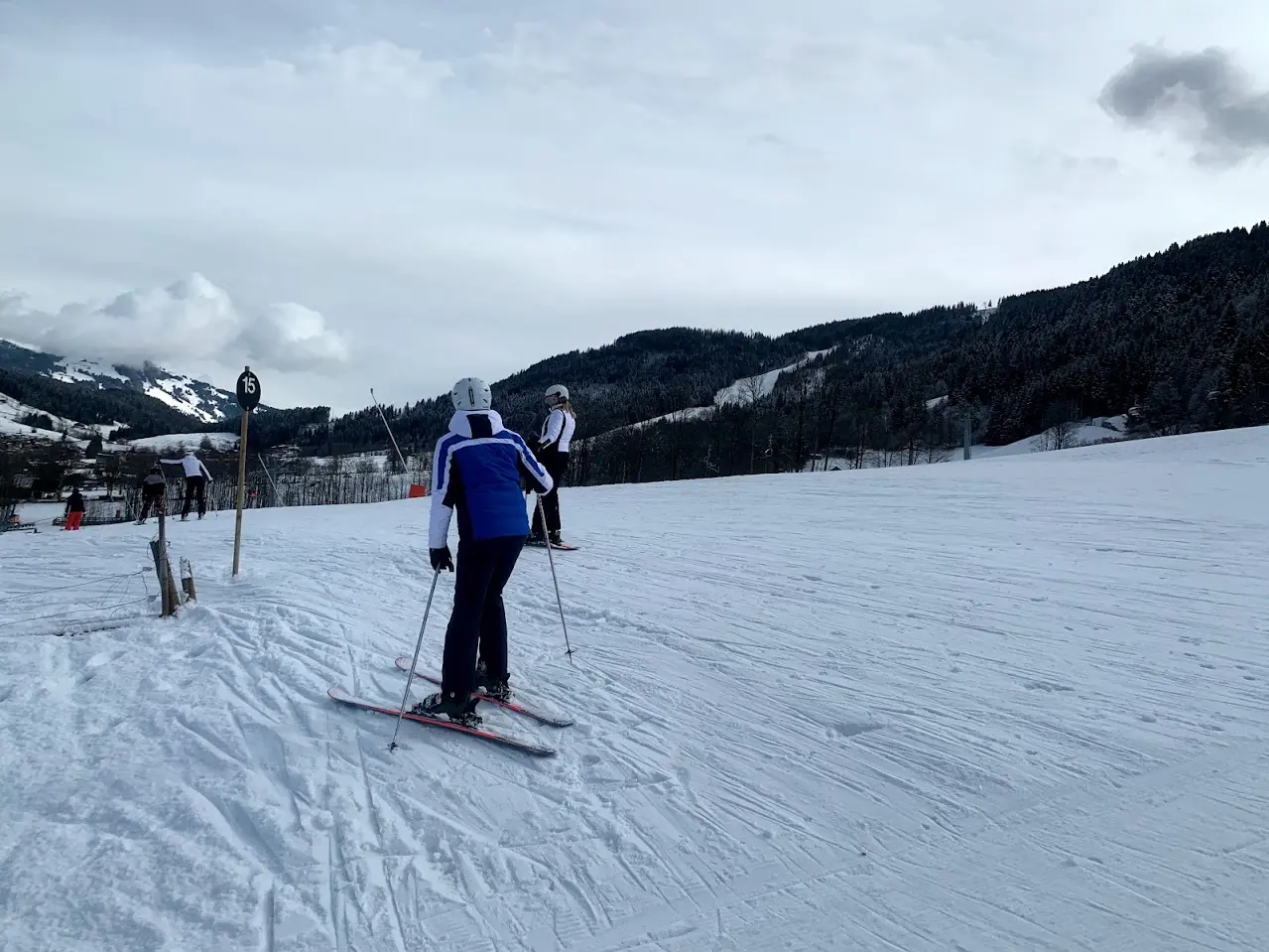Two skiers at marker 15 with a view over the valley and the wooded slopes