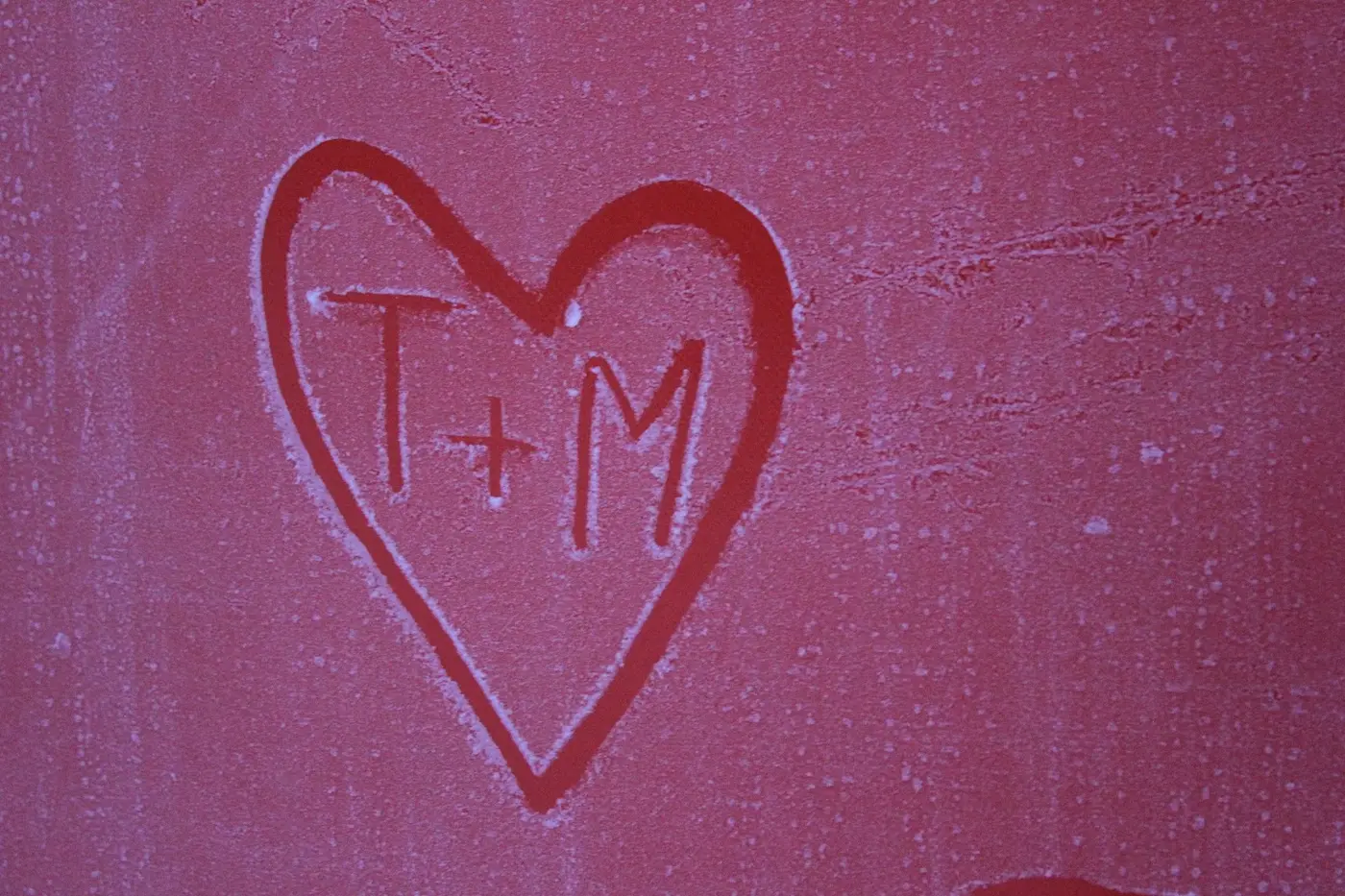 A heart with two letters drawn in frost on a red surface