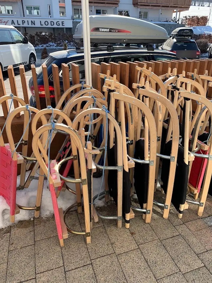 Row of wooden sleds with red and black seats, leaning against a wooden fence on a paved spot in winter