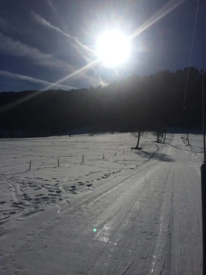 Słońce pod światło nad ośnieżoną ścieżką ze śladami i ciemnym grzbietem górskim
