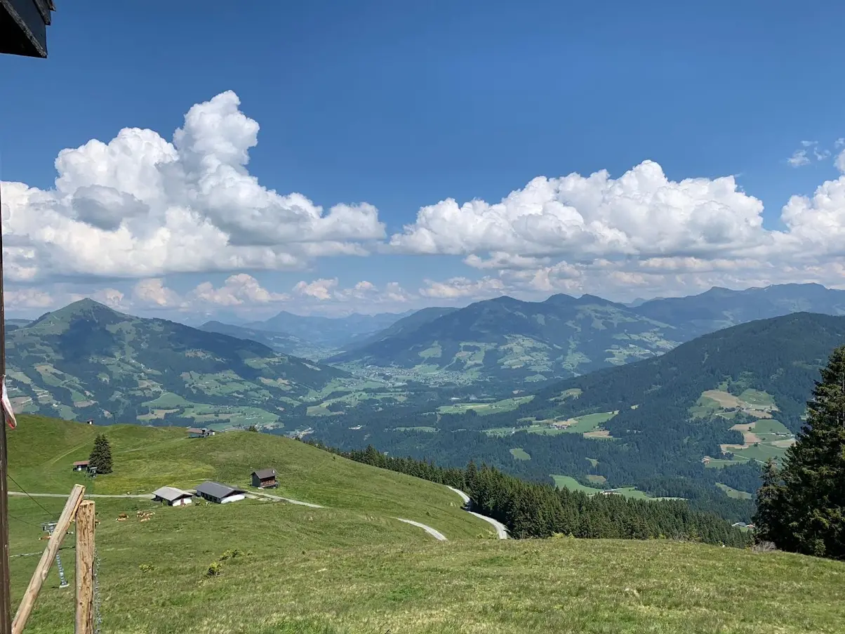 Pâturage alpin vert avec une vallée de montagne et des nuages au loin, avec une petite cabane sur la pente