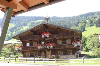 Wooden farmhouse with red geraniums at the windows and green mountain slopes behind