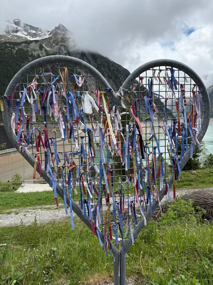 Metal heart full of colourful ribbons, with a turquoise reservoir and snow-capped mountains in the background