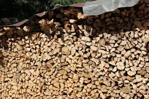 A large stack of split firewood under a roof