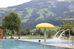 Outdoor pool with a yellow mushroom-shaped shower and water jets, with green mountain slopes behind