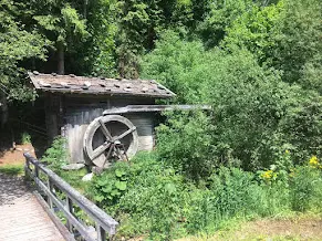 Old wooden watermill with a paddle wheel beside a stream, with a wooden bridge and greenery around it