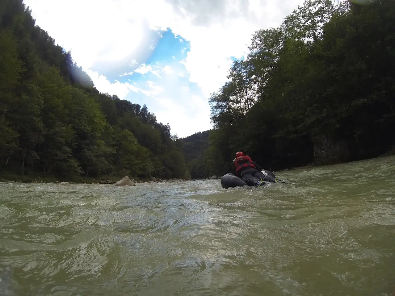 Tuber in a red helmet on a black inner tube in a mountain river between steep, wooded banks