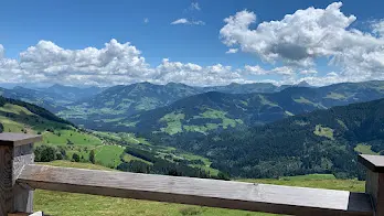 Summer view over green hills and mountain ranges from a wooden bench, with clouds in the sky
